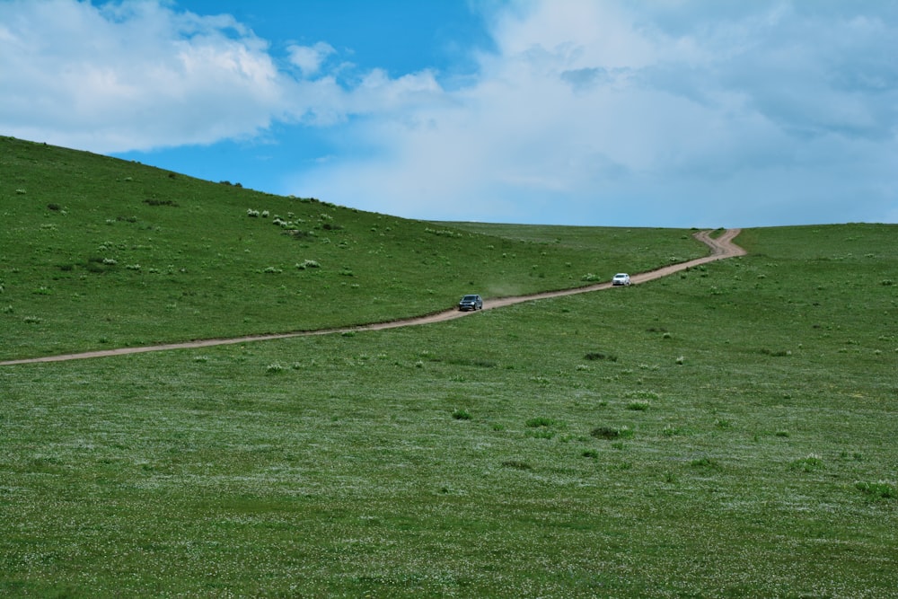 two cars driving down a dirt road on a grassy hill