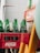 A collection of green Sprite bottles is arranged in a red Coca-Cola crate. The crate is positioned against a tiled wall, partially obscured by other objects. The bottles are empty, and the setup suggests a storage or recycling area.