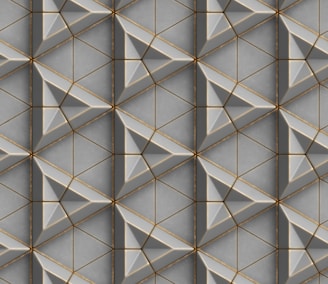 A repeating geometric pattern featuring interlocking triangles and diamond shapes with beveled edges. The design is composed of shades of gray and subtle gold accents, creating a three-dimensional effect.