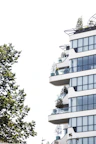 Exterior view of a small, modern building with balconies and greenery around.