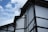 A traditional-style building with white walls and dark wooden beams is depicted against a partly cloudy sky. The roof features multiple angled sections, and there are antennas mounted on top. Electrical wires are visible, running across the building.