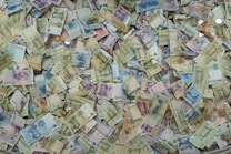 A large collection of various international banknotes and coins scattered randomly, showcasing a diverse range of currencies and denominations. The image reflects a chaotic but colorful mixture of paper money and coins from different countries.