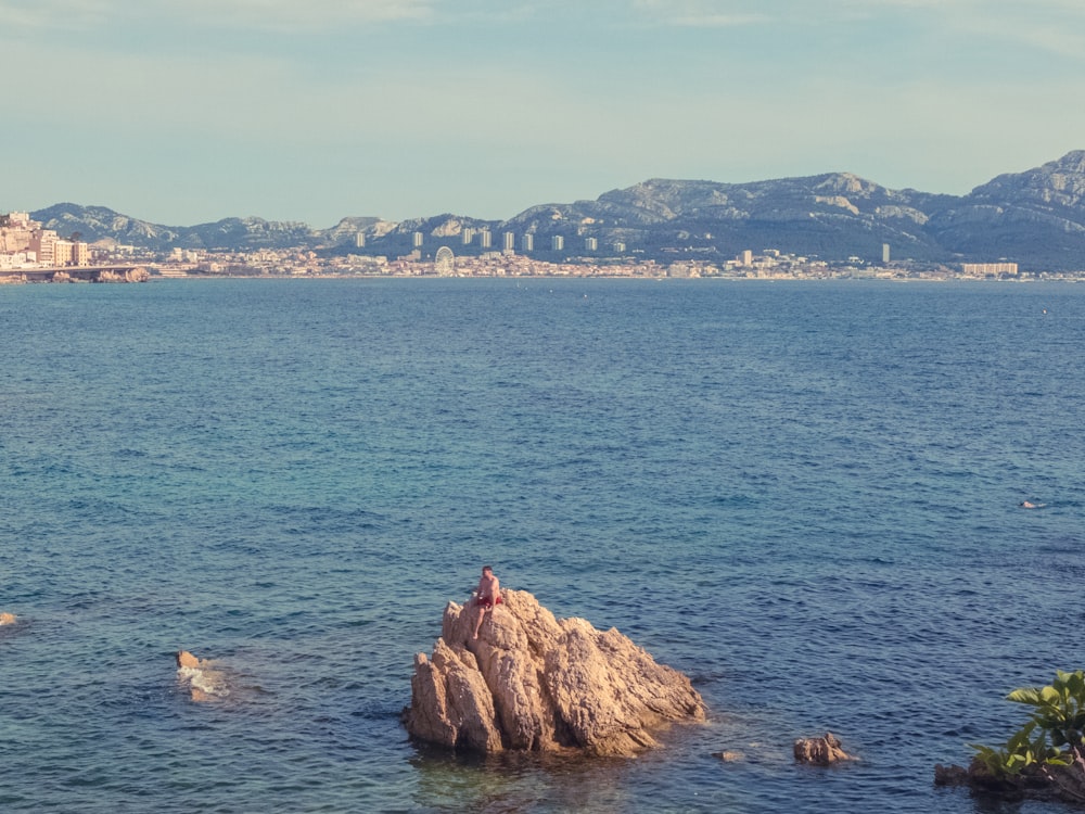 a person sitting on a rock in the middle of a body of water