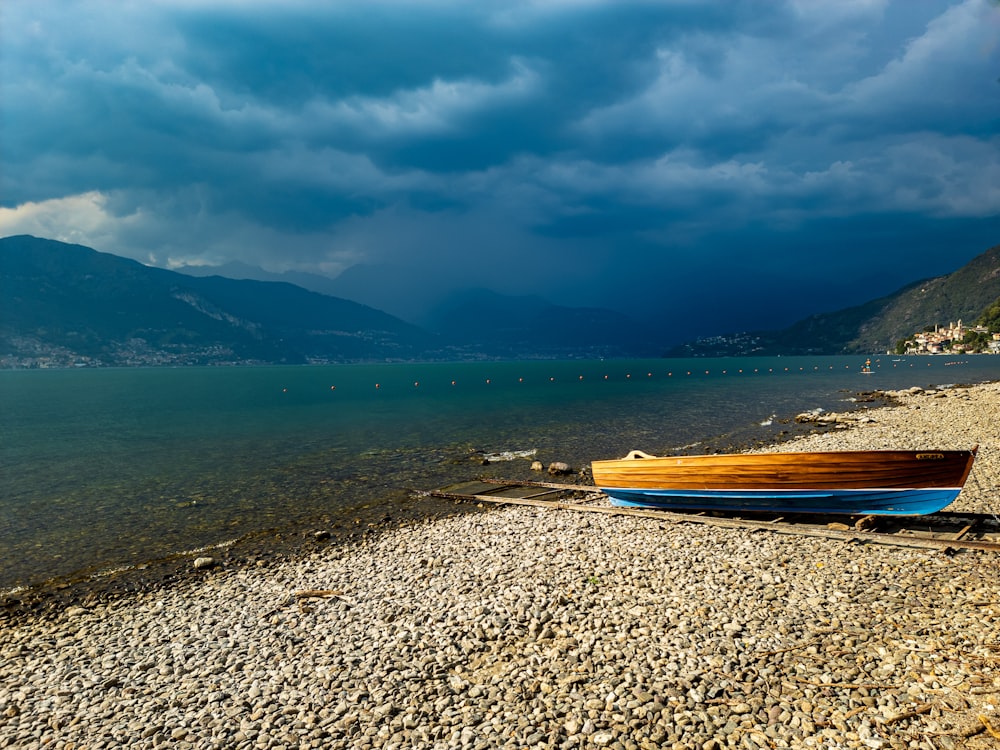 a boat sitting on the shore of a lake under a cloudy sky