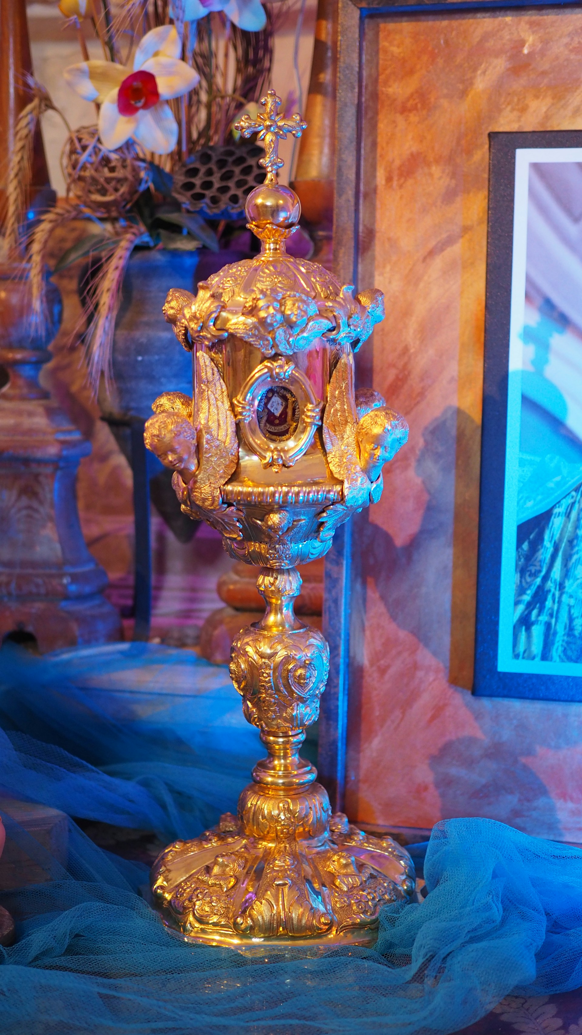 Close-up of a beautifully ornate chalice and paten resting on an embroidered altar cloth during a traditional Catholic ceremony.