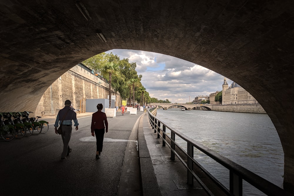 a couple of people walking down a street next to a river