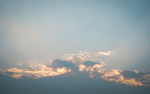 A serene sky with soft clouds parting to reveal a radiant light shining through.