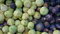 An assortment of fresh figs, consisting of green and purple varieties. The figs are in various states of ripeness and are closely packed, covering the entire frame.