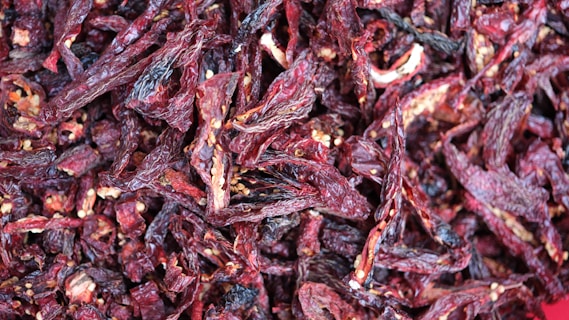 A dense pile of dried red chili peppers with visible seeds and wrinkled textures, suggesting they have been dehydrated. The peppers are overlapping and appear in various shades of deep red and maroon.