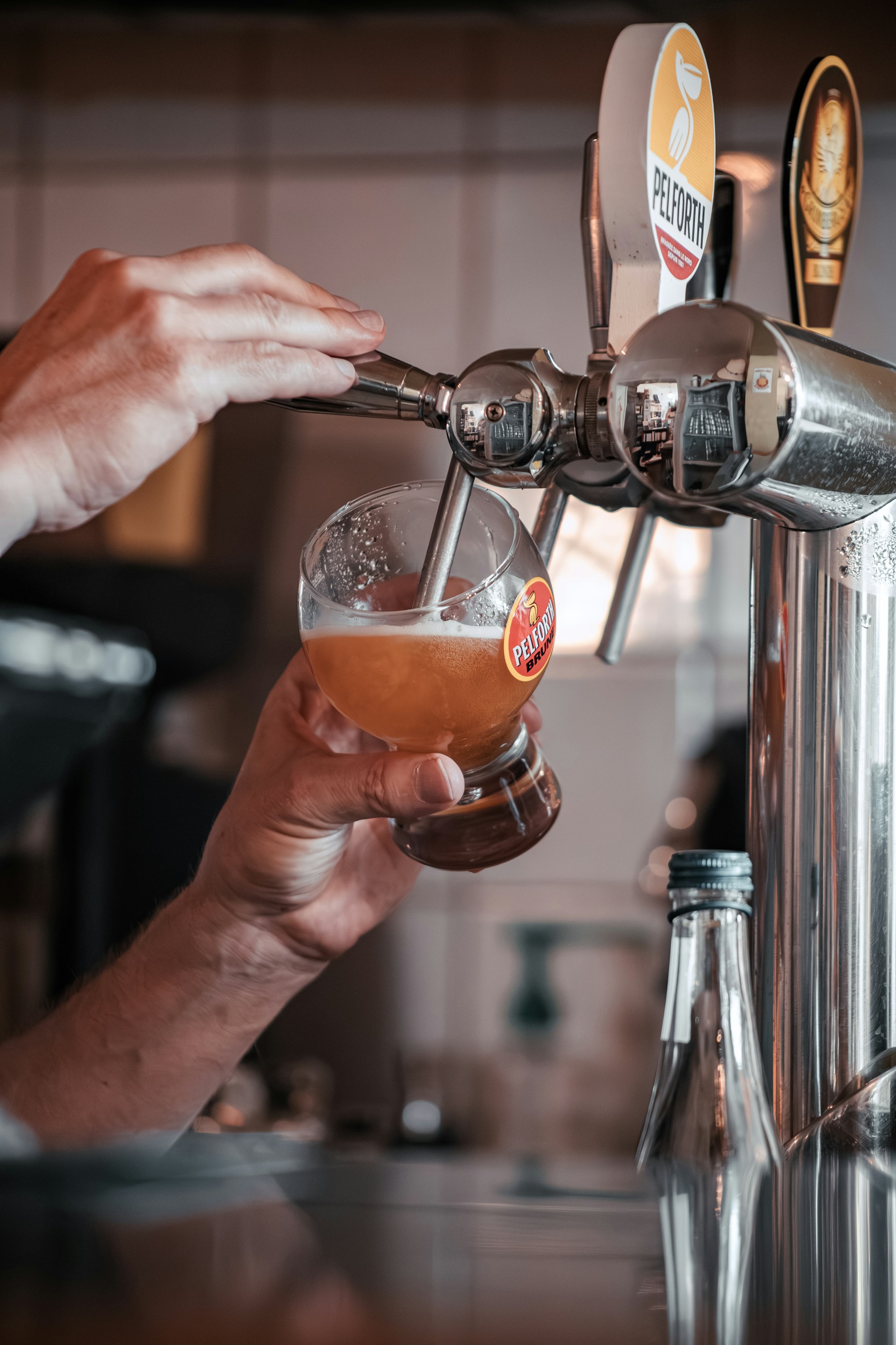 A refreshing cold beer being poured into a glass, with a background of the bustling bar cafeteria in the center of Córdoba.