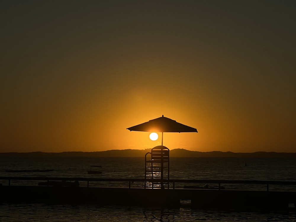 the sun is setting behind a beach umbrella