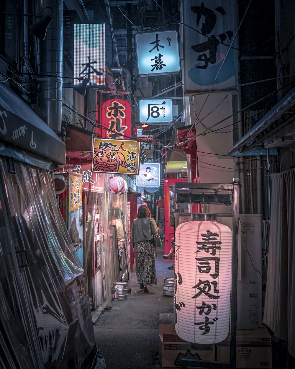 a narrow alley with signs and a woman walking down it