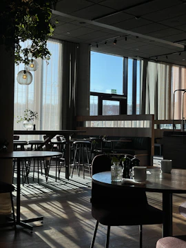 A warm, inviting coffee shop interior with sunlight streaming through large windows onto wooden tables.