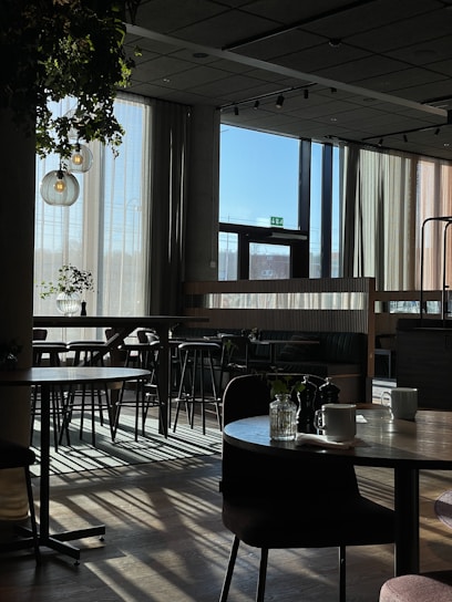 Cozy interior shot of offpark café with sunlight streaming through large windows onto wooden tables set for a community meal.