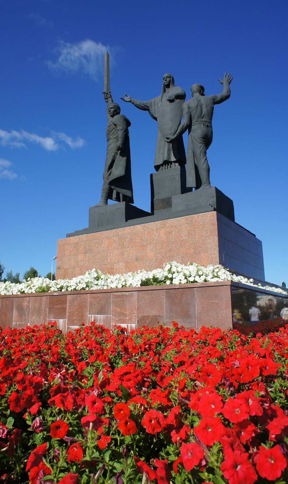 a statue of three men holding a sword in front of a field of red flowers