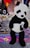 A large panda plush toy is displayed at a carnival booth. The booth features a sign advertising big prizes and colorful plush toys in the background, including a rainbow-colored toy. The environment is festive, with vibrant colors and promotional materials for winning prizes.
