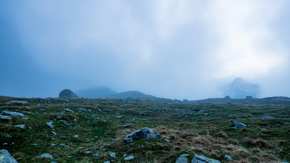 a grassy field with rocks and grass under a cloudy sky