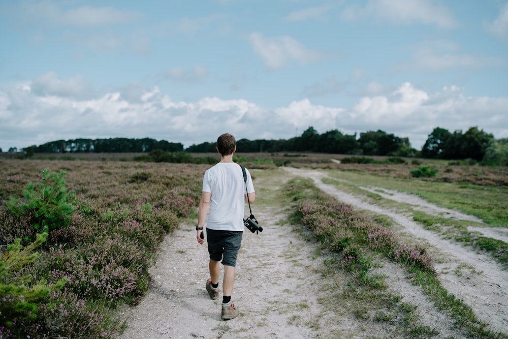 a man walking down a dirt path in a field
