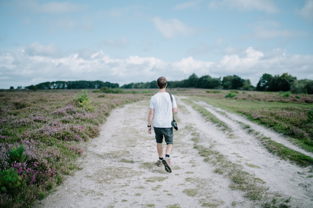 a man walking down a dirt road in a field