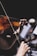 A close-up of a person playing a violin, with focus on the violin strings and bow. The background is blurred, suggesting a musical performance or practice session.