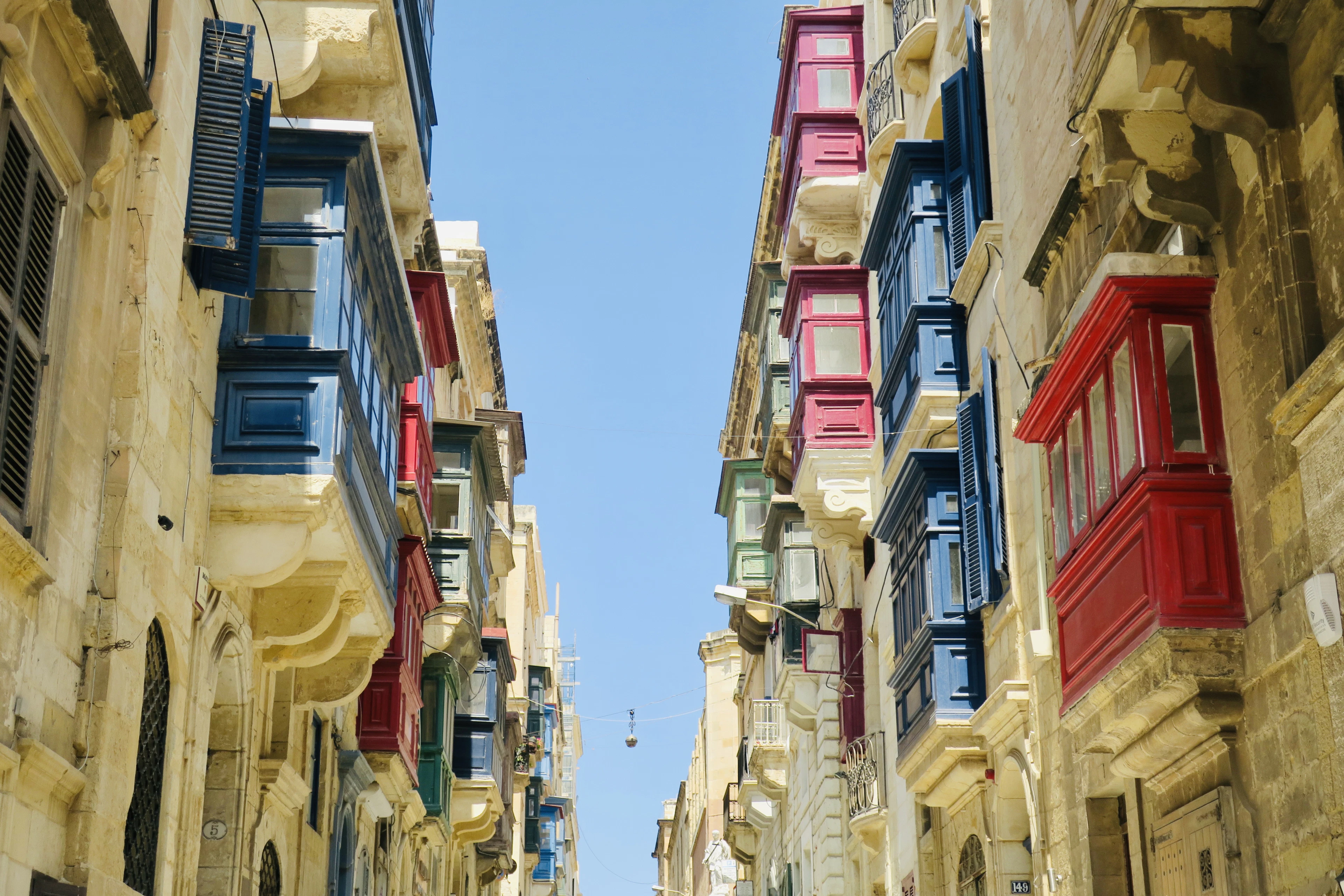 Rows of traditional enclosed timber balconies painted red, blue and green projecting from honey-coloured limestone facades on a narrow Valletta street.