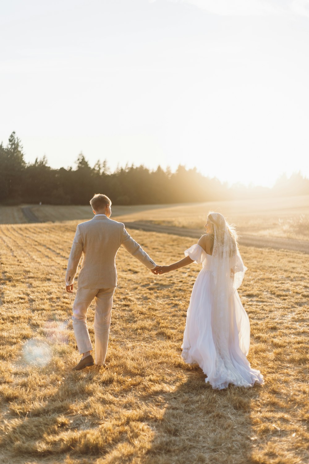 a bride and groom walking through a field holding hands