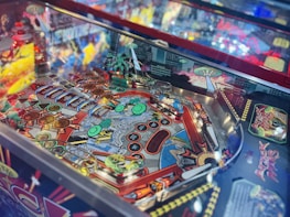 A colorful pinball machine with intricate artwork and vivid designs. The playfield is decorated with various circular targets, ramps, and bumpers, featuring comic-style illustrations and vibrant patterns.