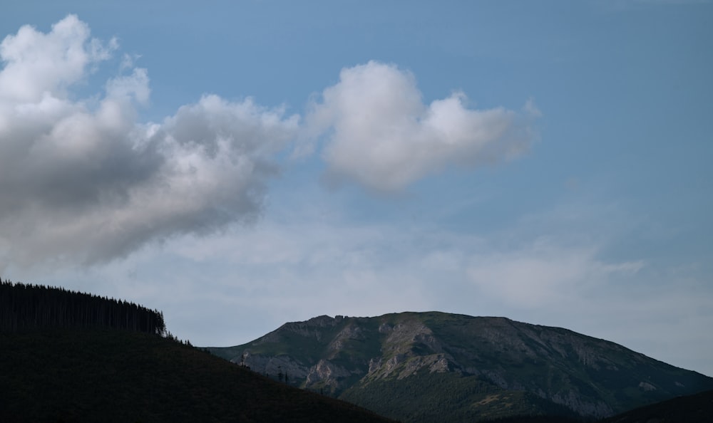 a hill with a tree on top of it under a cloudy sky