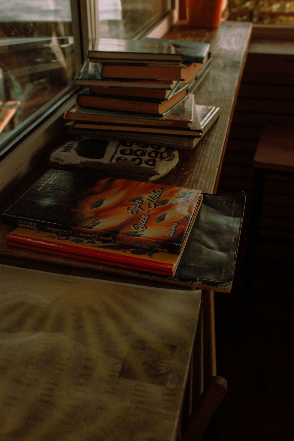 Una pila di libri seduti sopra un tavolo accanto a una finestra