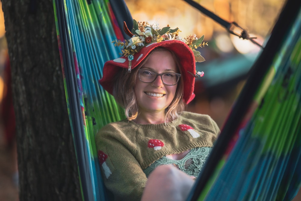 a woman wearing a red hat and glasses sitting in a hammock
