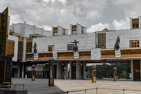A large, modern architectural structure with a geometric design. The building features tall windows with a mix of glass and concrete, and several sculptures are mounted prominently on the facade. There are decorative light fixtures and outdoor spaces that add to the imposing and grand appearance.