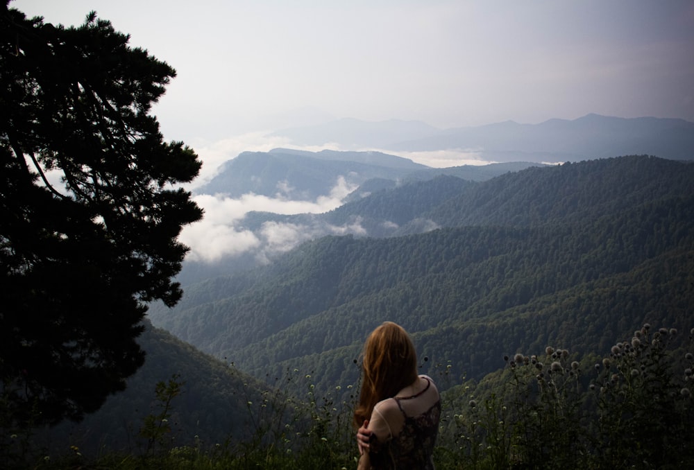 a woman standing on top of a lush green hillside