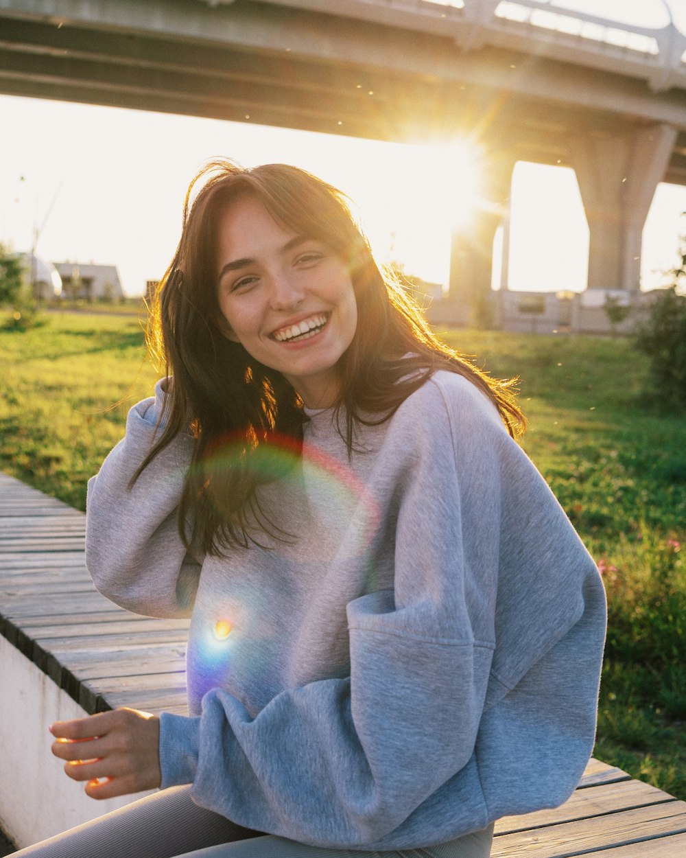 a woman sitting on a wooden bench in front of a bridge