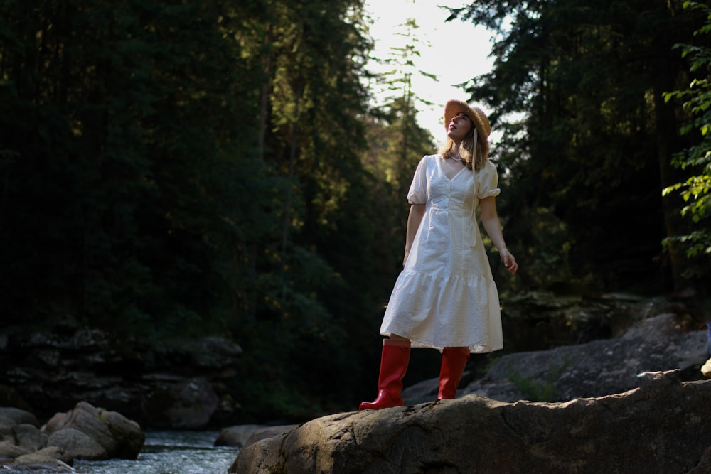 a woman in a white dress and red boots standing on a rock