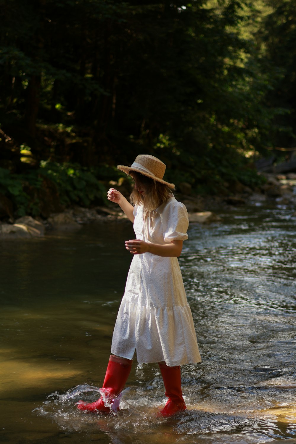 a woman in a white dress and red boots wading in a river
