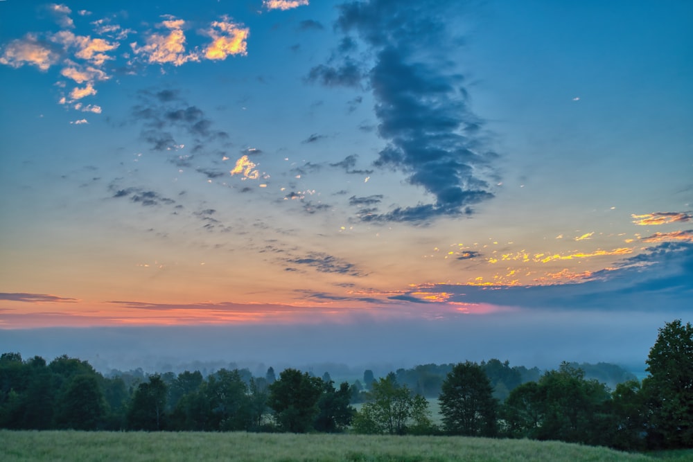 the sun is setting over a field with trees