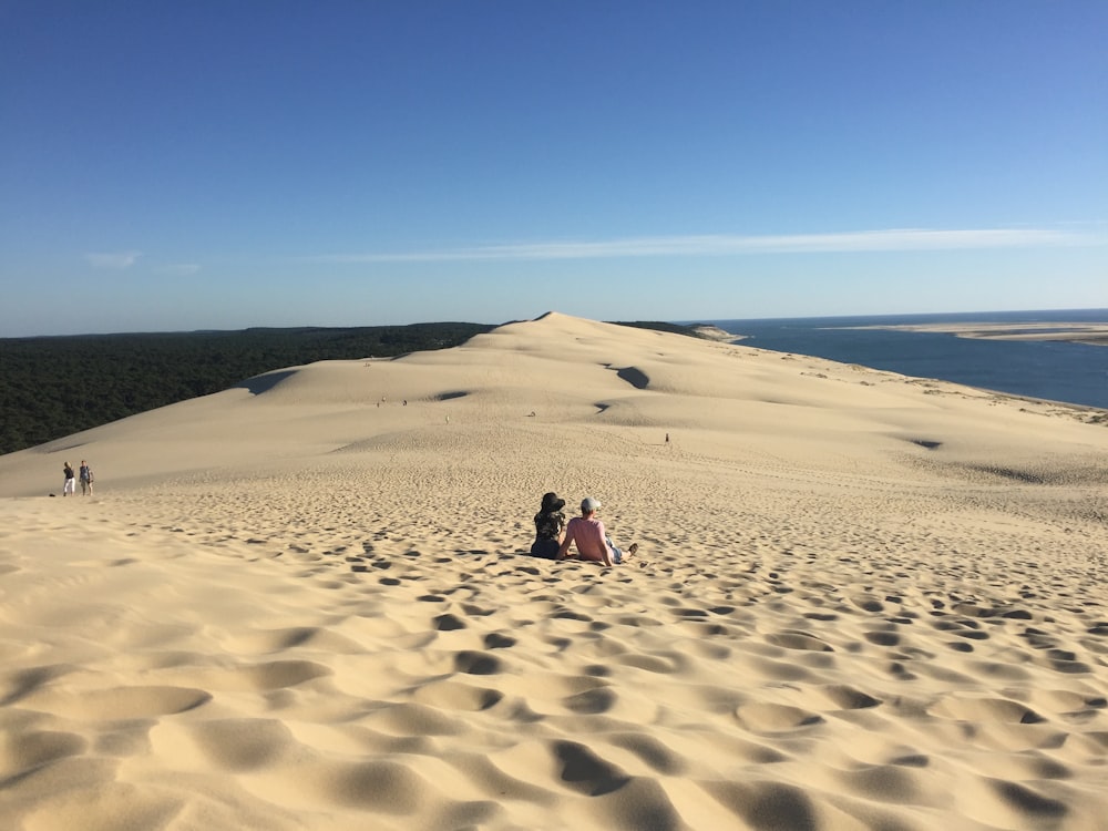 a group of people sitting on top of a sand dune