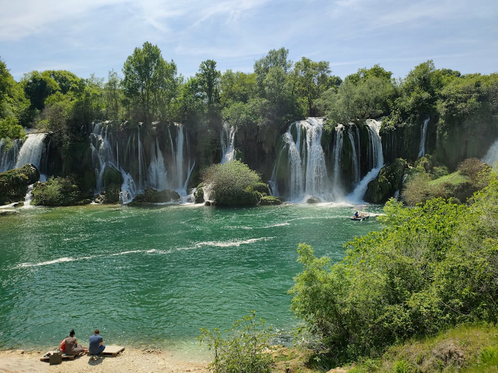 two people sitting on a bench in front of a waterfall