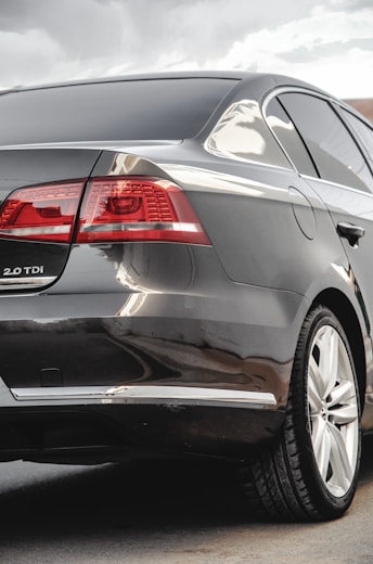 The image captures the rear view of a sleek, dark-colored sedan with tinted windows. The car appears modern and well-maintained, showcasing its taillights, rear badge indicating '2.0 TDI', and a clean, reflective surface with minor reflections.