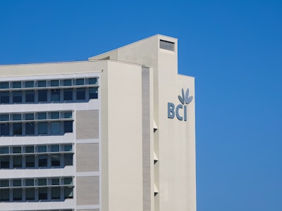 A modern building with multiple windows and a logo that includes the letters 'BCI' and a leaf motif. The structure is light-colored and set against a clear blue sky.