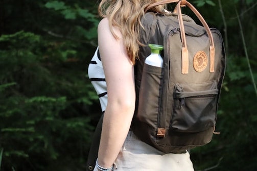 Close-up of the backpack’s side elastic pocket holding a water bottle beside green foliage.