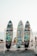 Three colorful surfboards with vibrant graffiti-style artwork are displayed on a wooden rack. Each board has a unique design featuring abstract and cartoonish images against the backdrop of a sandy beach with people in the distance and the ocean visible under a clear sky.