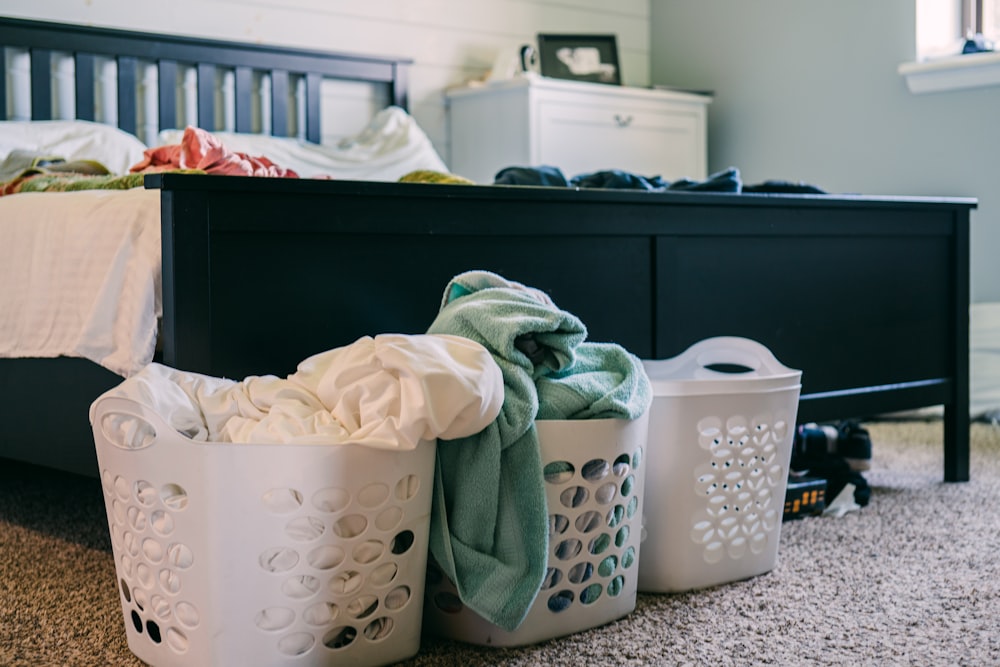 three laundry baskets sitting on the floor next to a bed