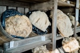 Several large pieces of cheese wrapped in black plastic are placed in wooden barrels on shelves. Each cheese wheel has a corresponding number tag, indicating their catalogued status.