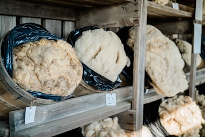 Several large pieces of cheese wrapped in black plastic are placed in wooden barrels on shelves. Each cheese wheel has a corresponding number tag, indicating their catalogued status.