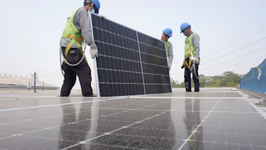 A close-up of a technician in protective gear inspecting solar panels on a sunny rooftop.