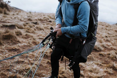 Close-up of a pilot adjusting their ergonomic harness before takeoff on a grassy slope.