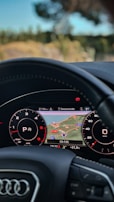 A close-up view of a car's dashboard featuring a digital display with a navigation map in the center. The display shows a location labeled CV-135, with surrounding roads and the names Benicarló and Pedregal. The dashboard includes detailed gauges, indicating speed and distance, surrounded by circular dials with numbers.
