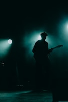 Silhouette of Kevin Emmanuel performing with a guitar under moody lighting.