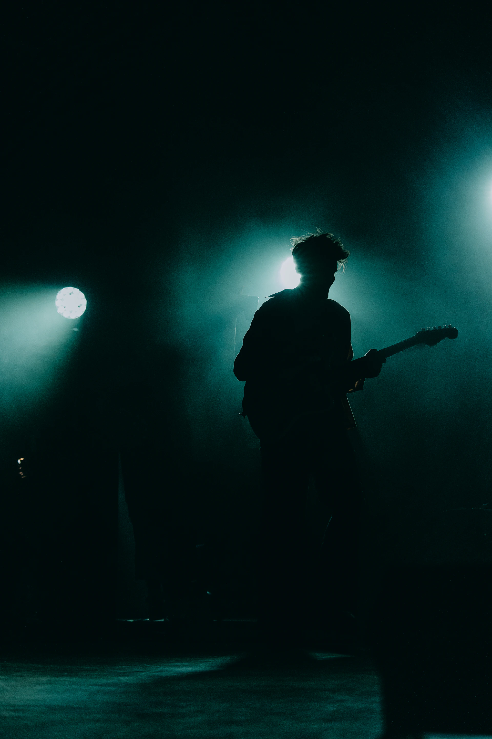 A moody, artistic shot of the lead singer silhouetted against colorful stage lights, evoking raw emotion.